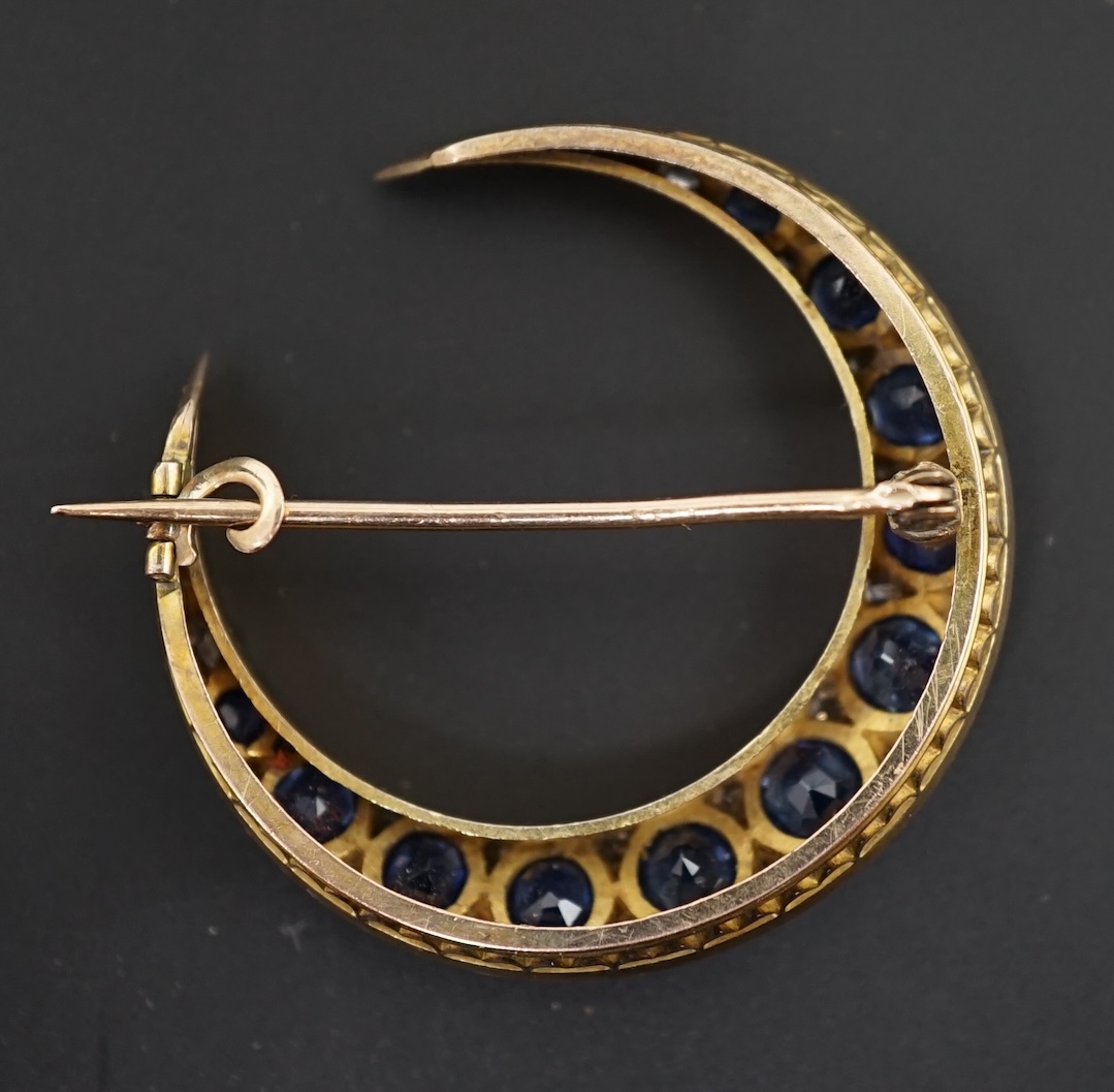 An early 20th century gold, graduated sapphire and diamond cluster set crescent brooch